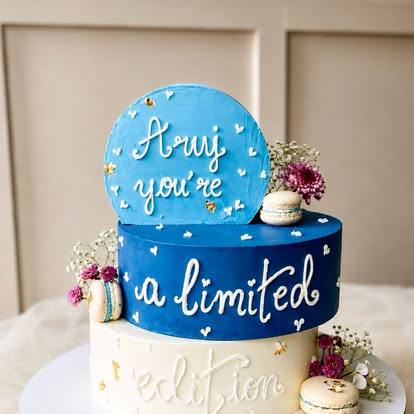 Blue and white birthday cake with hand-lettered message, macarons and flowers